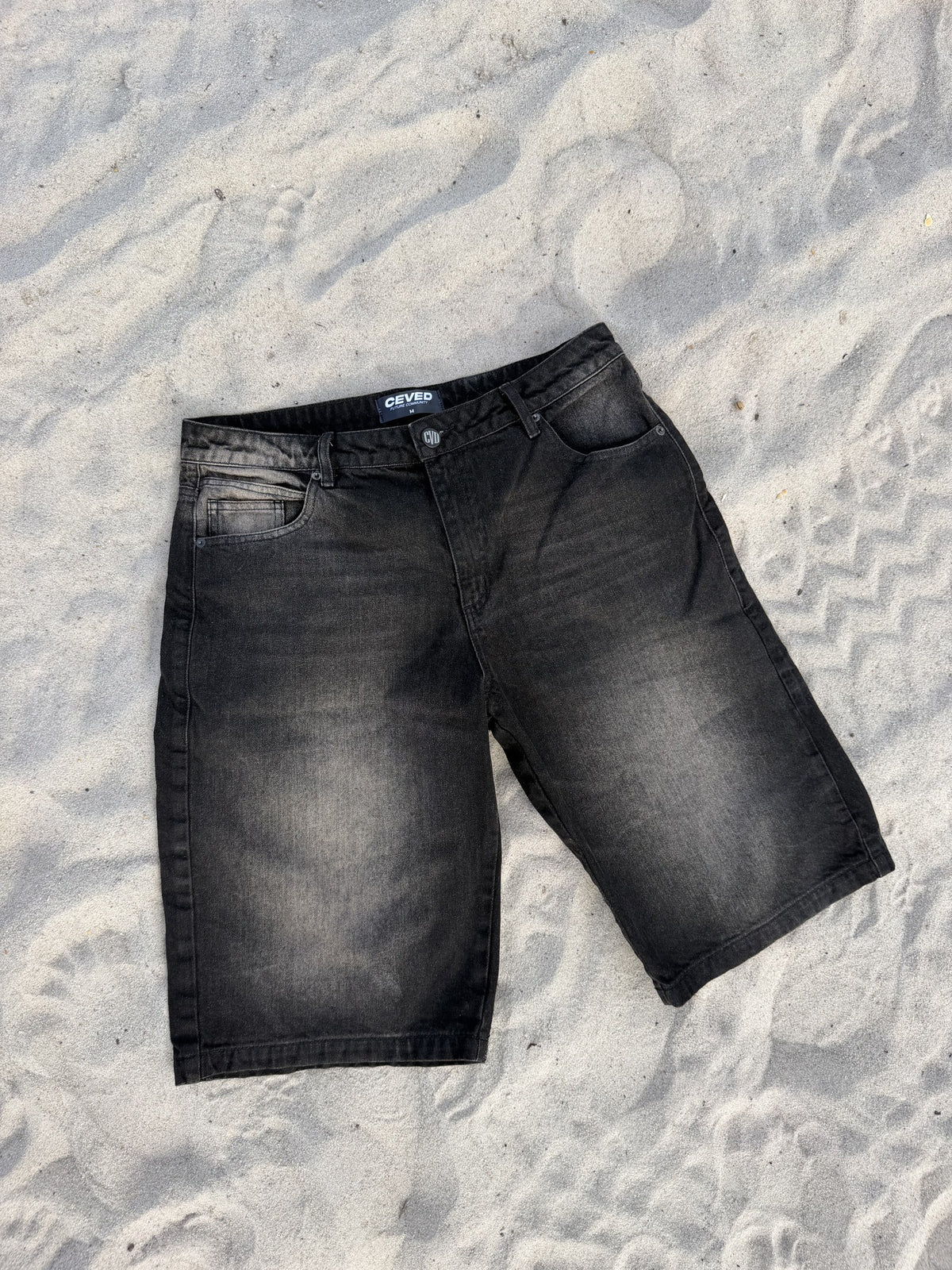 Bermuda Baggy Dirty F003 en denim negro con lavado dirty, vista completa sobre arena