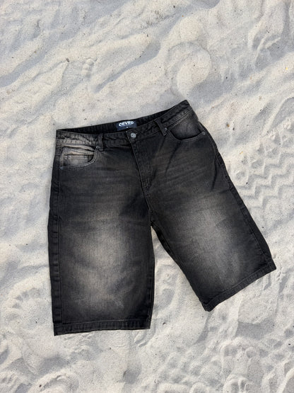 Bermuda Baggy Dirty F003 en denim negro con lavado dirty, vista completa sobre arena
